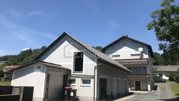 Graues Wohnhaus mit Satteldach und angeschlossener Garage unter blauem Himmel.