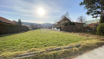Sonniges Grundstück mit grüner Wiese, umgeben von Häusern und mit Blick auf die Berge.