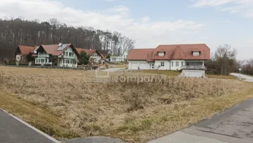 Weitläufiges Grundstück mit Blick auf umliegende Wohnhäuser und bewaldete Hügel unter bewölktem Himmel.