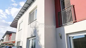 Seitenansicht eines modernen Hauses mit weißer und roter Fassade sowie einem französischen Balkon.