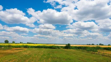 Weite Landschaft mit Feldern unter blauem Himmel und weißen Wolken, die eine friedliche Aussicht bietet.
