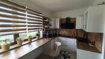 Moderne Küche mit weißen Schränken, Holzoptik-Arbeitsplatten und einem Fenster mit Jalousien.