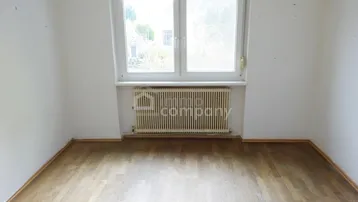 Unmöbliertes Schlafzimmer mit hellem Laminatboden und Fenster mit Blick ins Grüne.