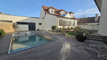 Außenbereich mit Swimmingpool, Holzterrasse, Steinfliesen und einem gepflegten Gartenbereich am Haus.