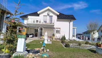 Hinteransicht des Hauses mit Garten, Terrasse und Balkon unter blauem Himmel.