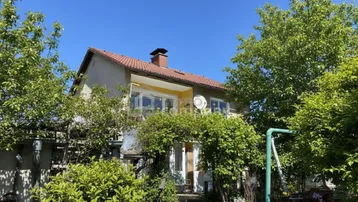 Traditionelles Einfamilienhaus mit rotem Ziegeldach und üppigem Grün im Vorgarten.