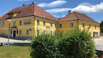 Historisches Gebäude mit leuchtend gelber Fassade und traditionellem Ziegeldach unter blauem Himmel.