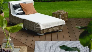 Gemütliche Sonnenliege auf einer Holzterrasse mit Blick ins Grüne und gepflegtem Rasen.