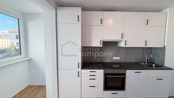 Moderne Einbauküche in Weiß mit dunkler Arbeitsplatte, integriertem Backofen und Fenster.