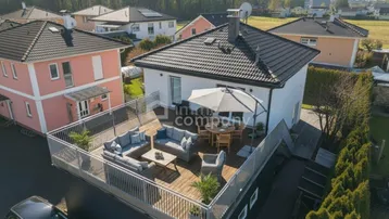 Luftaufnahme eines modernen Hauses mit großer, möblierter Dachterrasse und umliegenden Wohnhäusern.