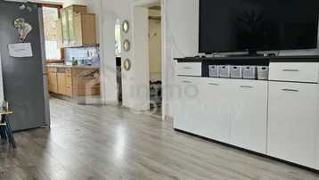 Heller Wohnbereich mit großem Fernseher, modernem Sideboard und Blick in die Küche.