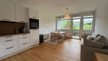 Helle Wohnküche mit Holzboden, weißen Schränken und Zugang zum Balkon mit Bergblick.