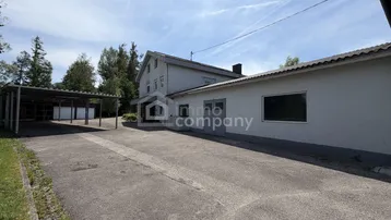 Rückansicht des Gebäudes mit großem asphaltierten Parkplatz und Carport-Struktur.