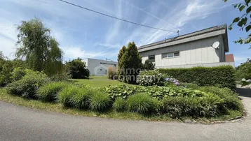 Gepflegter Vorgarten mit verschiedenen Sträuchern und Bäumen vor dem Gebäude.