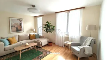 Helles Wohnzimmer mit beigem Sofa, Holzboden und Blick ins Grüne durch die Fenster.