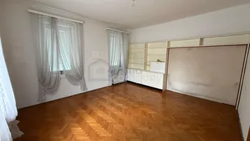 Geräumiges Zimmer mit Fischgrätparkett, großen Fenstern und integriertem Wandschrank.