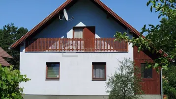 Frontansicht eines Einfamilienhauses mit Satteldach, Balkon und weißer Fassade.