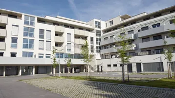 Modernes Mehrfamilienhaus mit weißer Fassade, großen Fenstern und Außenparkplätzen.