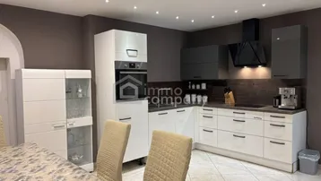 Moderne Küche mit weißen und grauen Schränken, integrierten Geräten und Essbereich.