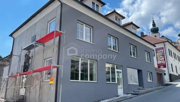 Gebäudeansicht mit grauer Fassade und Gerüst, das auf laufende Renovierungsarbeiten hinweist.