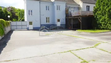 Rückseite eines Gebäudes mit großem gepflasterten Bereich und einer Holzterrasse.