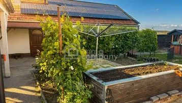Hausseite mit Solaranlage auf dem Dach und einem Hochbeet im sonnigen Gartenbereich.