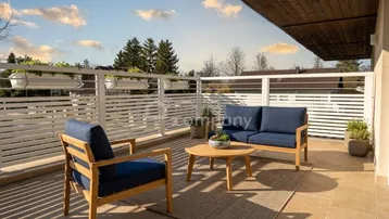 Geräumige Terrasse mit modernen Gartenmöbeln, weißem Geländer und Blick ins Grüne.