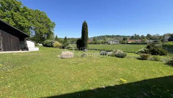 Großer, gepflegter Garten mit weitläufiger Rasenfläche, umgeben von Bäumen und ländlicher Idylle unter blauem Himmel.