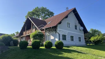 Traditionelles Haus mit Satteldach, Balkon und gepflegtem Garten in ländlicher Umgebung.