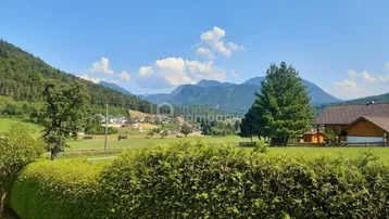 Panoramablick auf die umliegende Berglandschaft und ein idyllisches Dorf unter blauem Himmel.