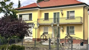 Elegante Villa mit gelber Fassade, rotem Ziegeldach und schmiedeeisernem Zaun im Vorgarten.