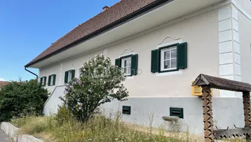 Traditionelles Haus mit grünen Fensterläden und gepflegter Fassade unter blauem Himmel.