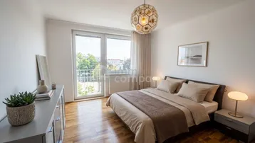 Helles Schlafzimmer mit Holzboden, modernem Bett und Zugang zu einem Balkon mit grüner Aussicht.