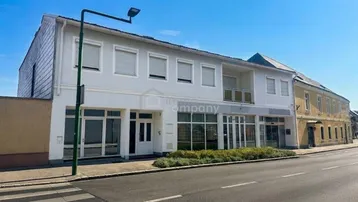 Gebäudeansicht mit Geschäftsflächen im Erdgeschoss und Wohnungen darüber an einer Straße.