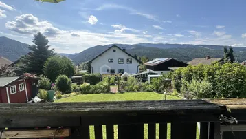 Weitblick vom Balkon über den grünen Garten und die malerische Berglandschaft.