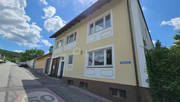 Gelbe Fassade eines Wohnhauses mit weißen Fensterrahmen unter blauem Himmel.