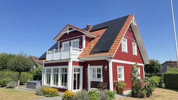 Rotes Einfamilienhaus mit weißem Balkon, Solaranlage auf dem Dach und gepflegtem Garten.