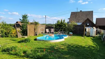Gepflegter Gartenbereich mit einem kleinen Pool, Liegestühlen und viel Grünfläche unter blauem Himmel.