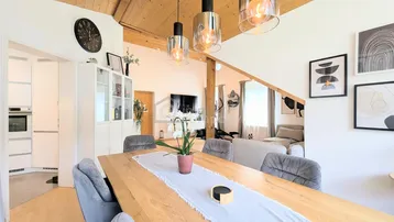 Heller Essbereich mit Holztisch, modernen Pendelleuchten und Blick in den Wohnbereich und die Küche.