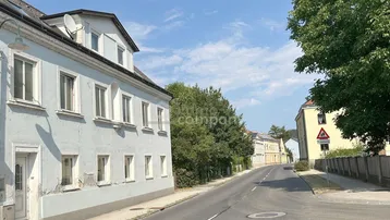 Alte Fassade eines Gebäudes an einer ruhigen Straße unter blauem Himmel.