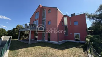 Rückseite des modernen Hauses mit großem Balkon, Rasenfläche und weitem Blick.