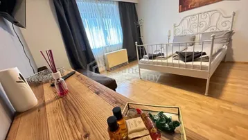 Helles Schlafzimmer mit Holzboden, weißem Metallbett und einem Schreibtisch am Fenster.