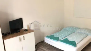 Helles Schlafzimmer mit Doppelbett, TV-Möbel und Laminatboden in einfacher Ausstattung.