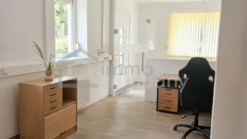Helles Büro mit Laminatboden, einem Fenster mit Blick ins Grüne und moderner Büroeinrichtung.