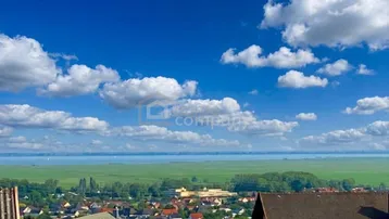 Weitläufiger Panoramablick über den See, grüne Felder und eine Stadt unter strahlend blauem Himmel.