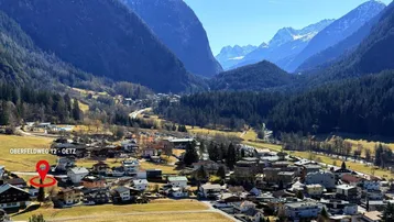 Panoramablick auf die alpine Landschaft mit einem Dorf, umgeben von grünen Tälern und schneebedeckten Bergen.