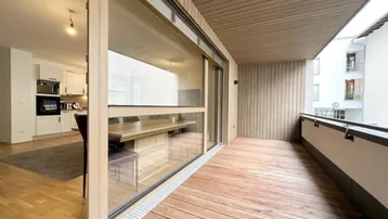 Geräumiger Balkon mit Holzboden und Blick in den offenen Wohnbereich, perfekt für entspannte Stunden im Freien.