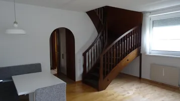 Heller Wohnbereich mit Esstisch, Holztreppe und Parkettboden, der in die obere Etage führt.