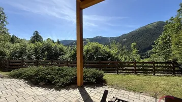 Geräumige gepflasterte Terrasse mit Holzdach und weitem Blick auf die umliegende Berglandschaft.