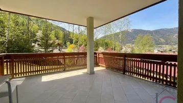 Geräumige überdachte Terrasse mit Fliesenboden, Holzbalkon und malerischem Bergblick.